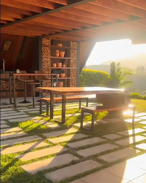 A área externa coberta, com a mesa de madeira e a lenha, ao sol da tarde