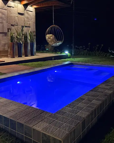 A piscina iluminada à noite, com a poltrona suspensa ao fundo